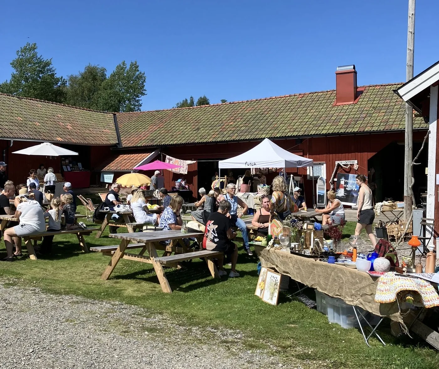 Somrig marknad med loppisbord och besökare framför ladan